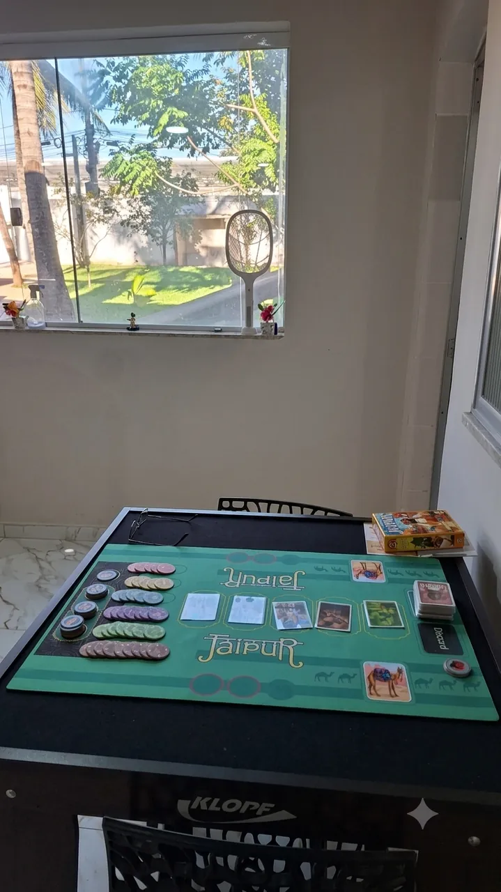 Mesa de jogos de tabuleiro na sala de convivência, com janela para o jardim